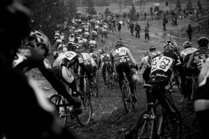 Cyclists racing down a muddy track. Black and white photograph taken from the back of the pack.